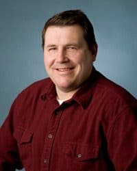 From the desk of Tony Carey photo of Tony. He's wearing a maroon colored long sleeve, button down shirt.