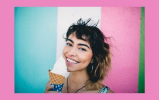 Maintaining frozen custard machines image. Young woman holding an ice cream cone. She is smiling and in front of a blue, white and pink background.