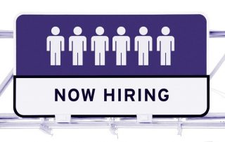 Ice cream shop staffing solutions image sign with six white icons of a person with purple background. Underneath are the words in black text "NOW HIRING" with white background.